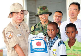 ジブチ干ばつにともない、日本船主協会から提供された支援物 資をDouda小学校（ジブチ）の子供たちへ手渡しする派遣海賊対処 行動航空隊司令（左）