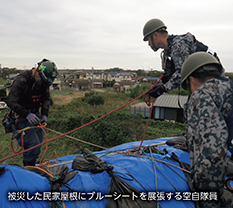 被災した民家屋根にブルーシートを展張する空自隊員