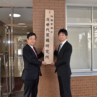 防衛装備庁次世代装備研究所の看板を設置する大西防衛大臣政務官と土志田次世代装備研究所長